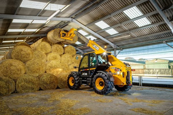 Télescopique agricole JCB 542-70 Agri Pro empilant des bottes de paille rondes dans un hangar.