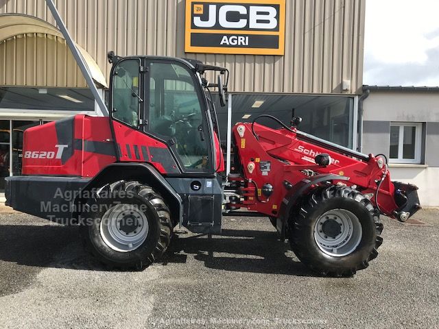 Chargeuse télescopique articulée rouge Schäffer 8620 T vue de profil, stationnée devant une concession JCB AGRI.