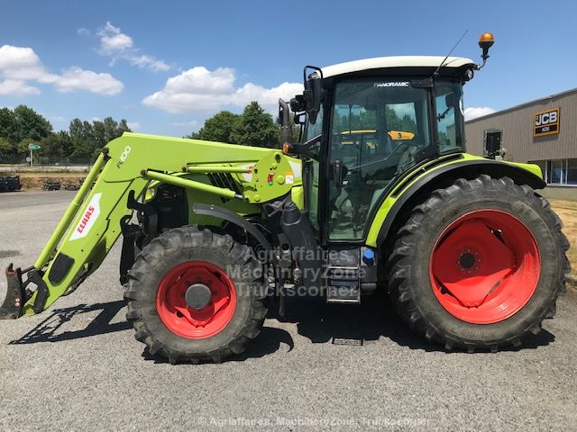 Tracteur agricole Claas Arion 420 vert clair de profil, équipé d'un chargeur frontal Claas FL100, stationné sur un parking d'occasion devant une concession.